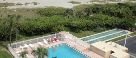 A swimming pool with lounge chairs, a tennis court, and a view of the beach.
