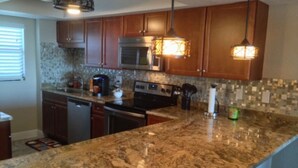Una cocina con encimeras de granito, armarios de madera, electrodomésticos de acero inoxidable e iluminación colgante.