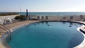 Ein Pool mit Blick auf den Ozean, umgeben von Liegestühlen und Sonnenschirmen.