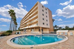 A hotel with a pool, palm trees, and a clear sky.