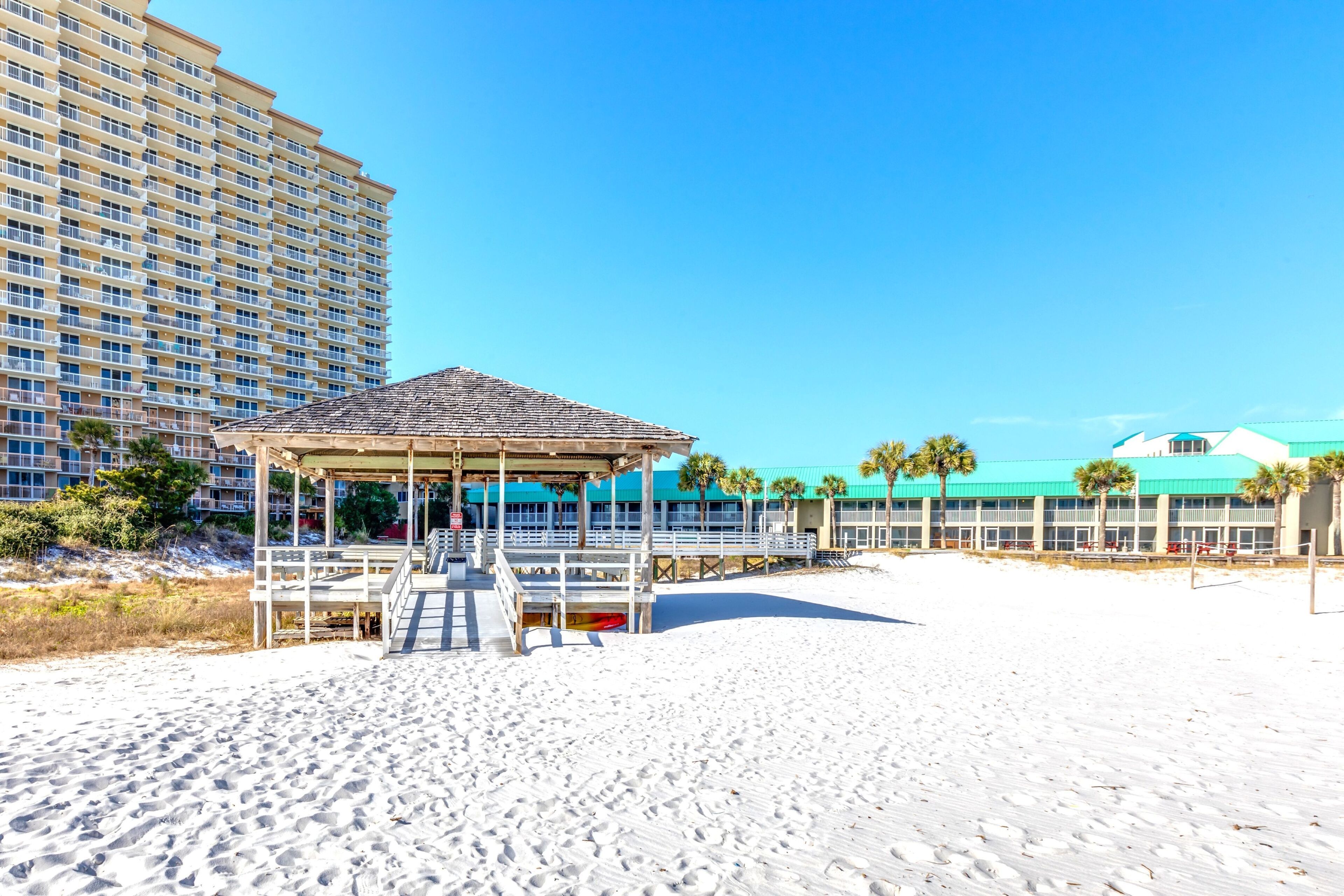 A beach with a gazebo, a tall building, and a building with a green roof.