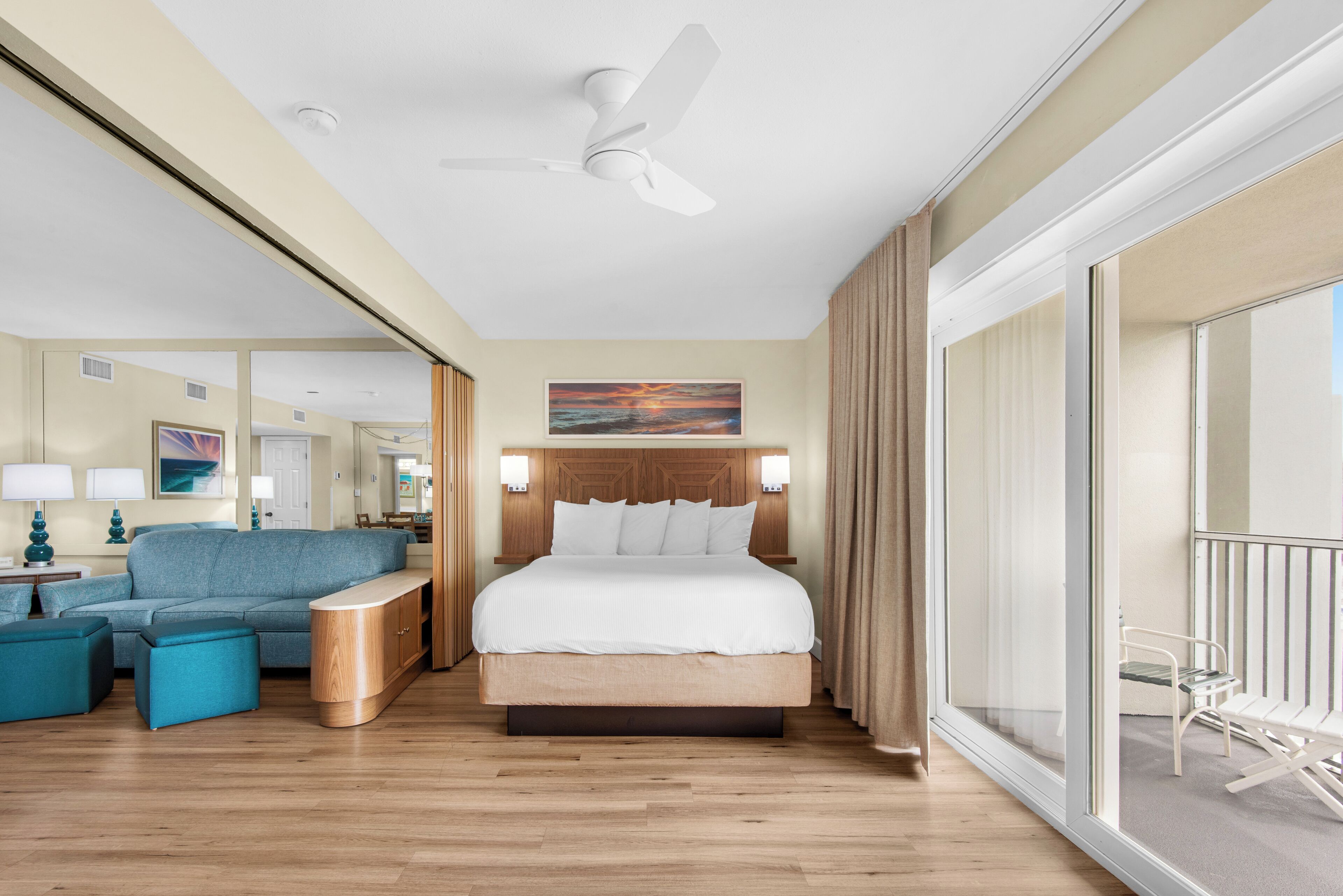 A hotel room with a bed, a sofa, a nightstand, a ceiling fan, and a large window.