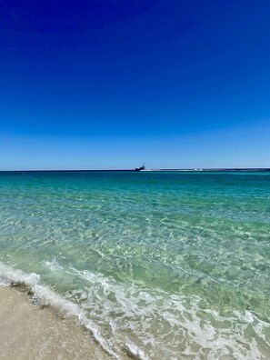 A beach with clear turquoise water and a boat in the distance. - Destin Holiday Beach Resort (Destin)
