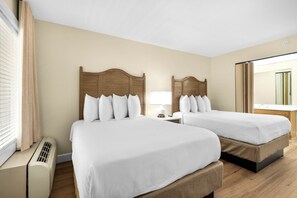 A hotel room with two beds, a bedside table, a lamp, and a window with curtains.