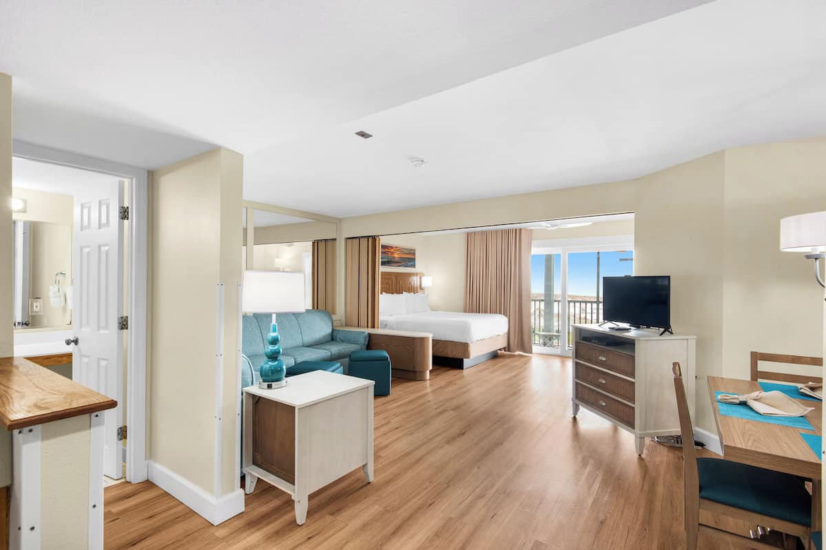 A hotel room with a bed, a sofa, a desk, a TV, and a balcony with a view.