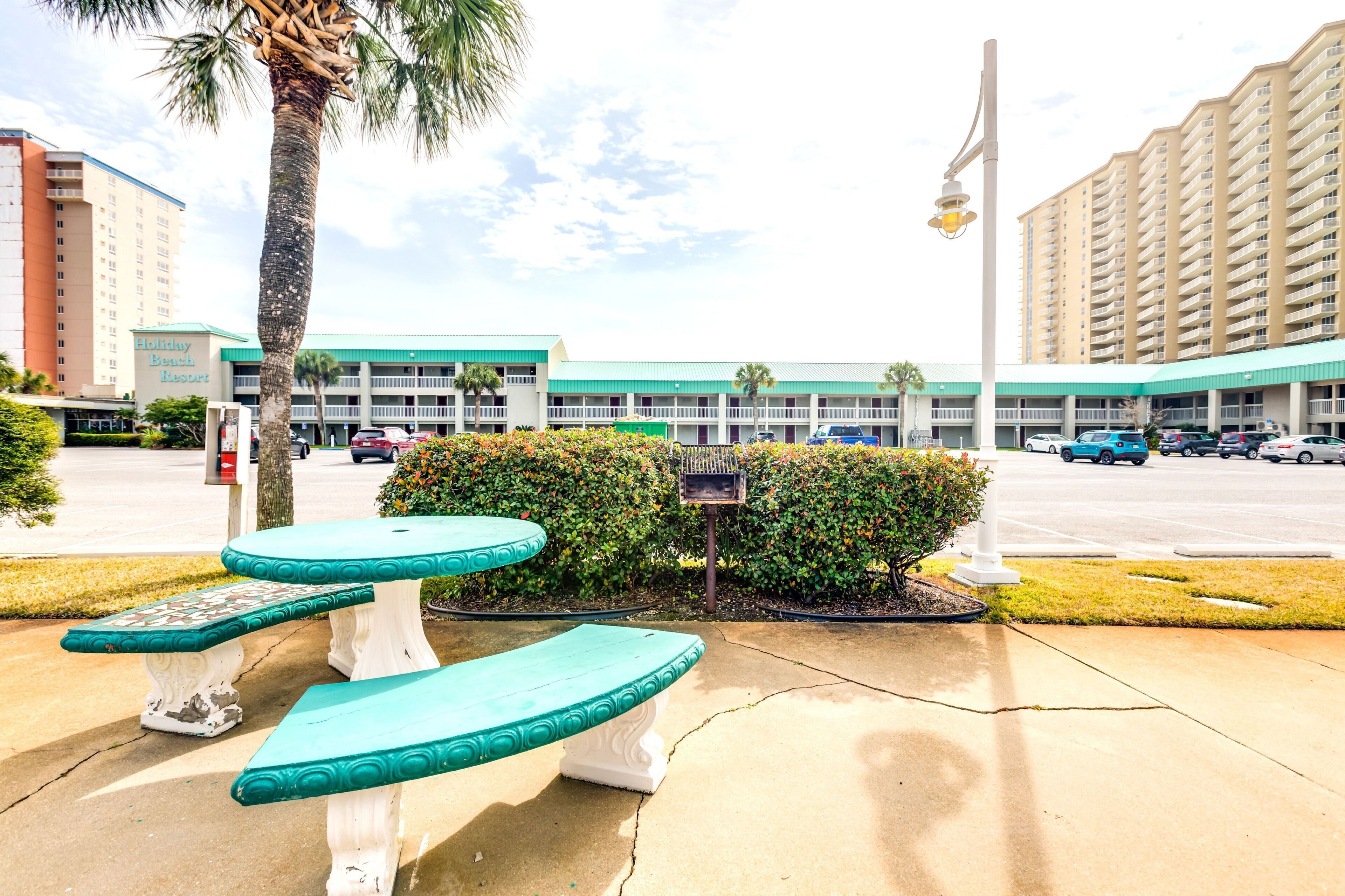 Un hotel con fachada verde y blanca, varios espacios de estacionamiento y una palmera.
