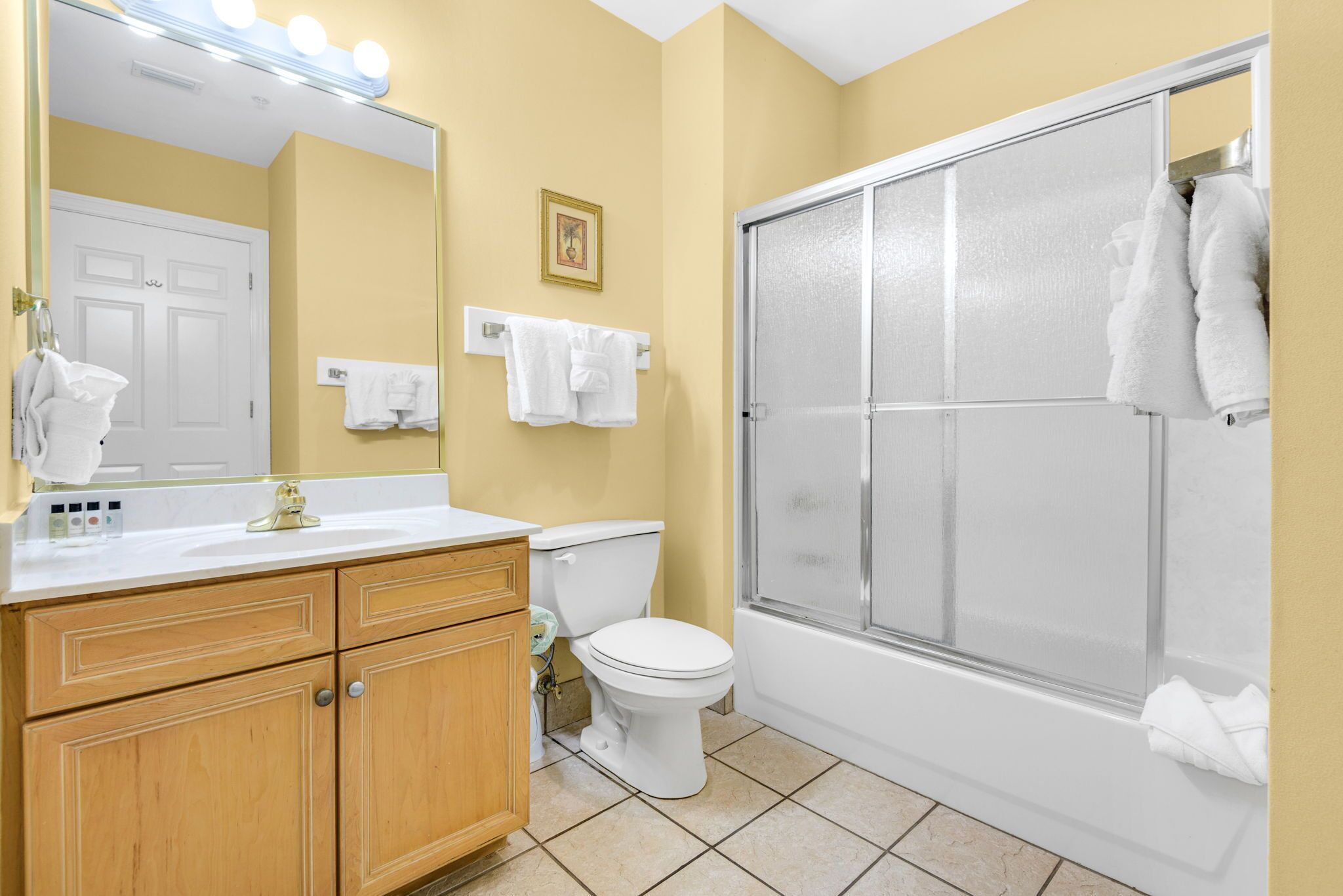 Un baño con inodoro, lavamanos con espejo y ducha con puerta de vidrio.