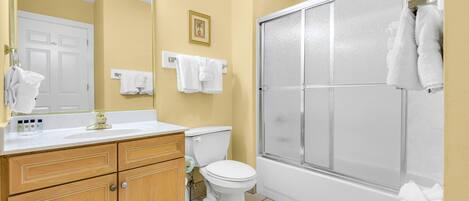 Un baño con inodoro, lavamanos con espejo y ducha con puerta de vidrio.