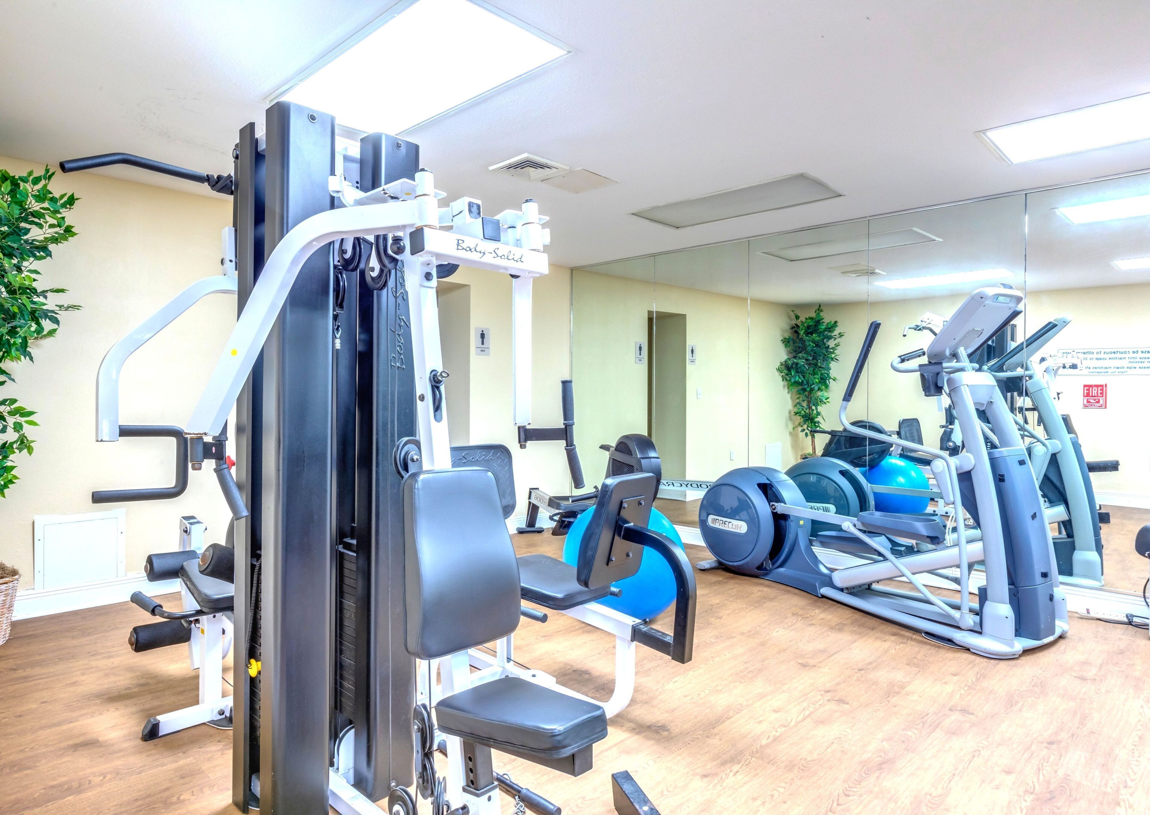 A gym with various exercise equipment, including a weight machine, treadmills, and a blue medicine ball.
