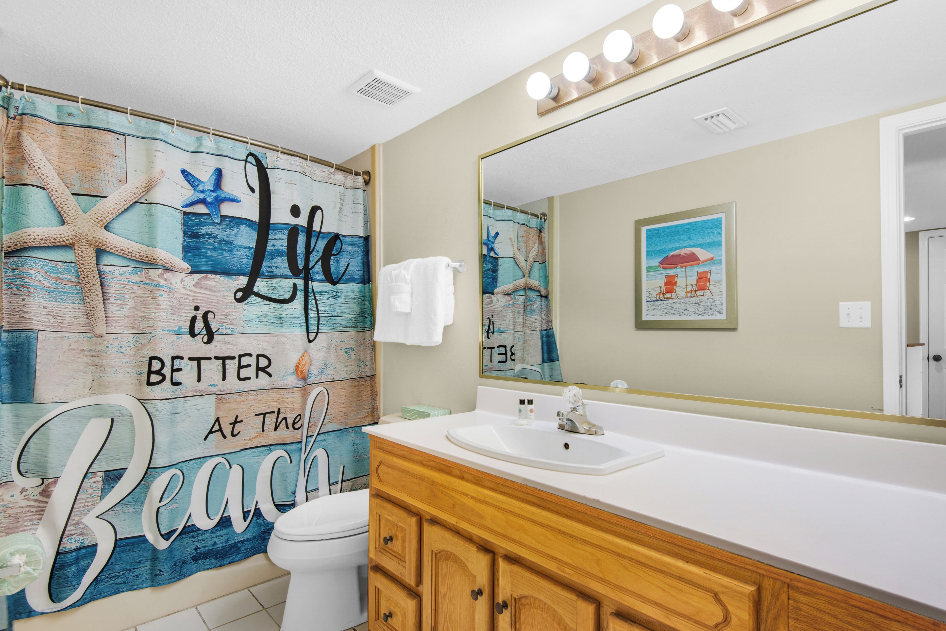 A bathroom with a beach-themed mural, a white sink, wooden cabinets, and a large mirror.