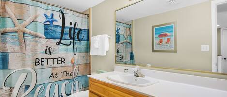 A bathroom with a beach-themed mural, a white sink, wooden cabinets, and a large mirror.