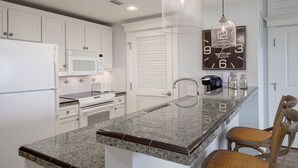 A modern kitchen with white cabinetry, a granite countertop, a stainless steel range, a microwave, a toaster, and a hanging pendant light. - 1 bedroom, 2 Full bath condo in Sandestin  (Miramar Beach)