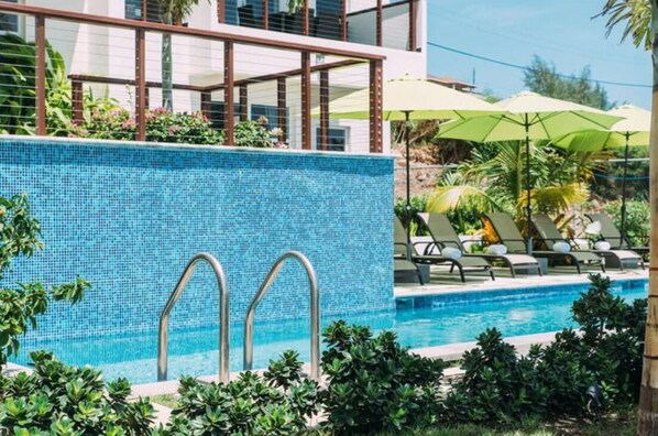 Una piscina con pared de azulejos, sillas de descanso y sombrillas.