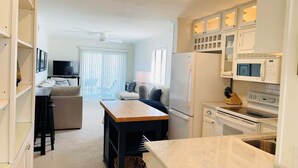 A compact living space with a kitchenette, a dining area, and a seating area with a television. - Cozy 2BR condo at Holden Beach, perfect for a family getaway! (Holden Beach)