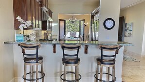 A modern kitchen with a central island, wooden bar stools, and a clock on the wall. - Experience Aloha Avila luxury executive home in San Luis Bay Estates (Avila Beach)