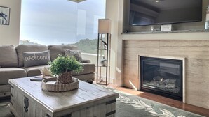 A living room with a sofa, a coffee table with a plant, a fireplace, and a TV mounted on the wall. - Experience Aloha Avila luxury executive home in San Luis Bay Estates (Avila Beach)