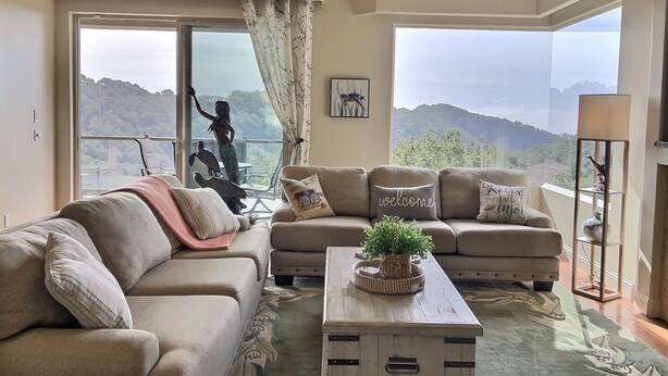 A spacious living room with a large window offering a scenic mountain view, a cozy sofa set, and a wooden coffee table. - Experience Aloha Avila luxury executive home in San Luis Bay Estates (Avila Beach)
