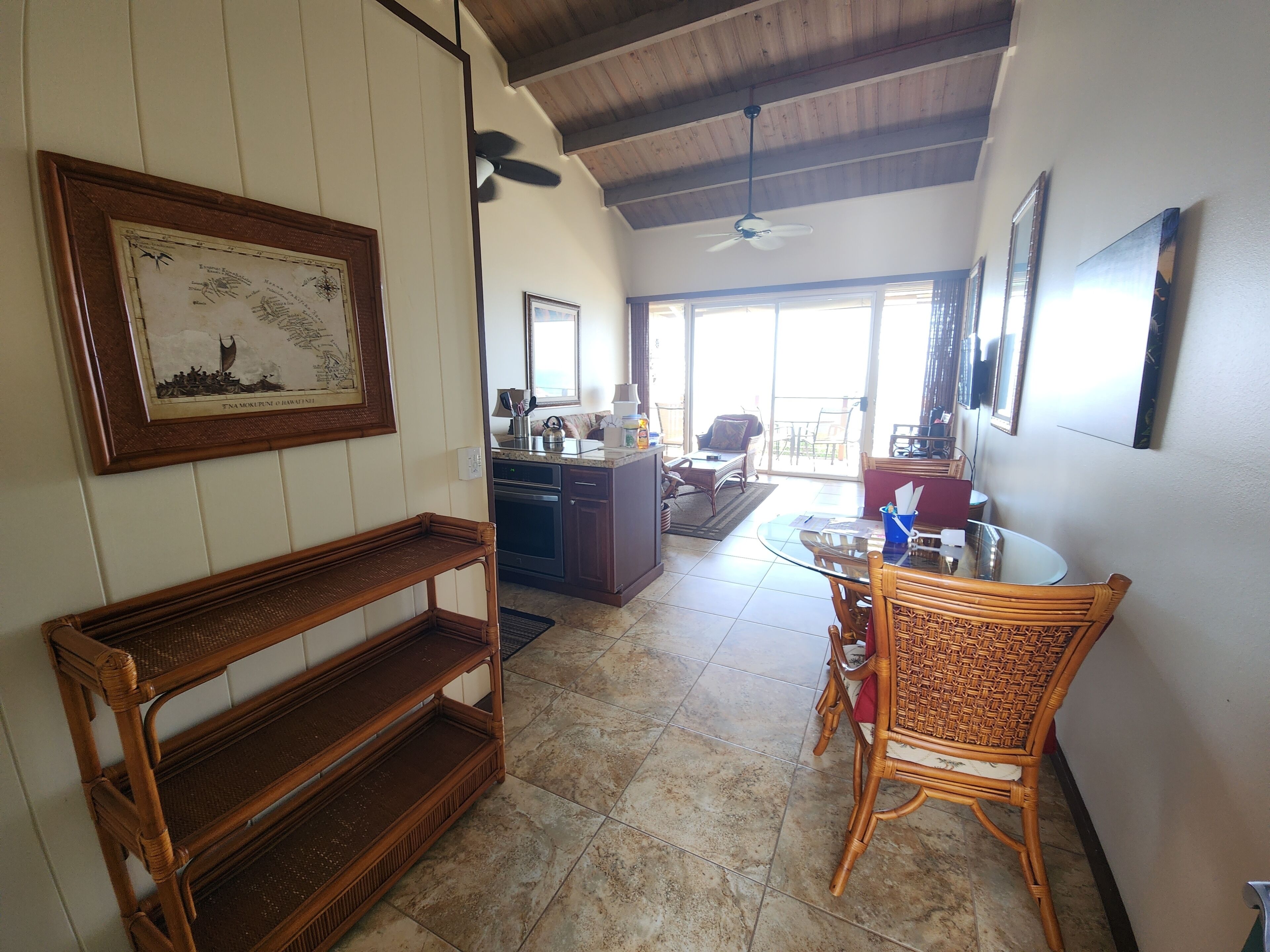 A spacious living area with a dining table, wicker chairs, a wooden bench, and a ceiling fan.