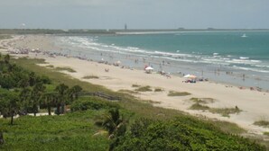 A beach with a long stretch of sand, a few umbrellas, and a few people.
