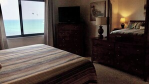 A hotel room with a bed, a dresser, a television, and a view of the ocean.