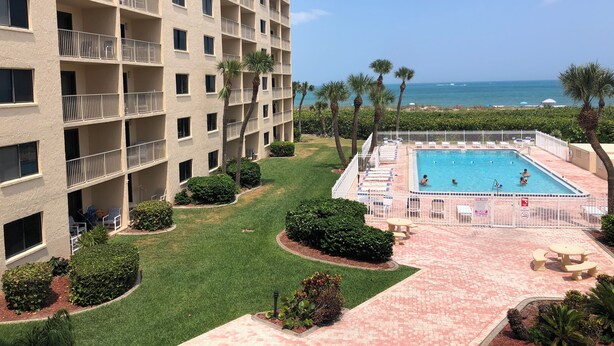 Un hotel su più piani con area piscina, palme e vista sull'oceano.