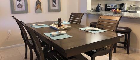 A dining area with a wooden table, chairs, and a kitchen in the background.