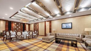 A hotel lobby with a checkered carpet, a seating area with sofas and chairs, a dining area with round tables and chairs, and a wall-mounted television. - Golden Bay International Hotel (Meizhou)