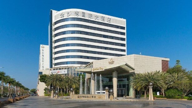 A modern hotel with a curved facade, a prominent entrance with a canopy, and a clear sky. - Golden Bay International Hotel (Meizhou)
