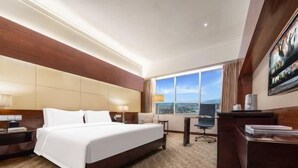 A hotel room with a large bed, a desk, a chair, and a view of the outdoors. - Golden Bay International Hotel (Meizhou)