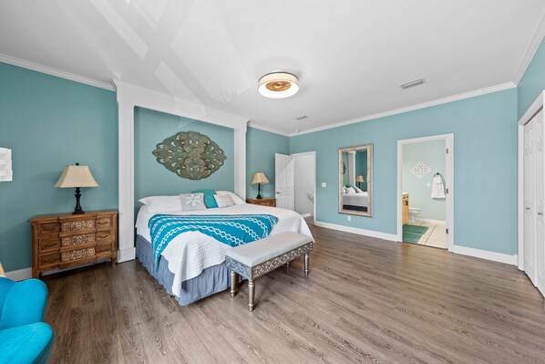 Een slaapkamer met een bed, een bankje, een dressoir, een lamp en een spiegel.