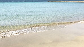 Ein Strand mit klarem Wasser, einem Sandufer und einem entfernten Wellenbrecher.