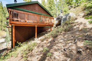 Eine Holzhütte mit Balkon, umgeben von Bäumen und einer felsigen Hügelkuppe.