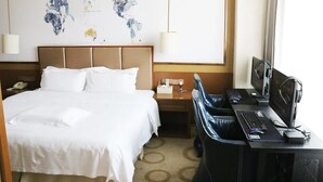 Ein Hotelzimmer mit Bett, Schreibtisch, Computer und einer Weltkarte an der Wand.