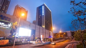 Ein modernes Hotelgebäude mit einer auffälligen vertikalen Beschilderung, umgeben von weiteren Hochhäusern und einer belebten Straße mit fließendem Verkehr.
