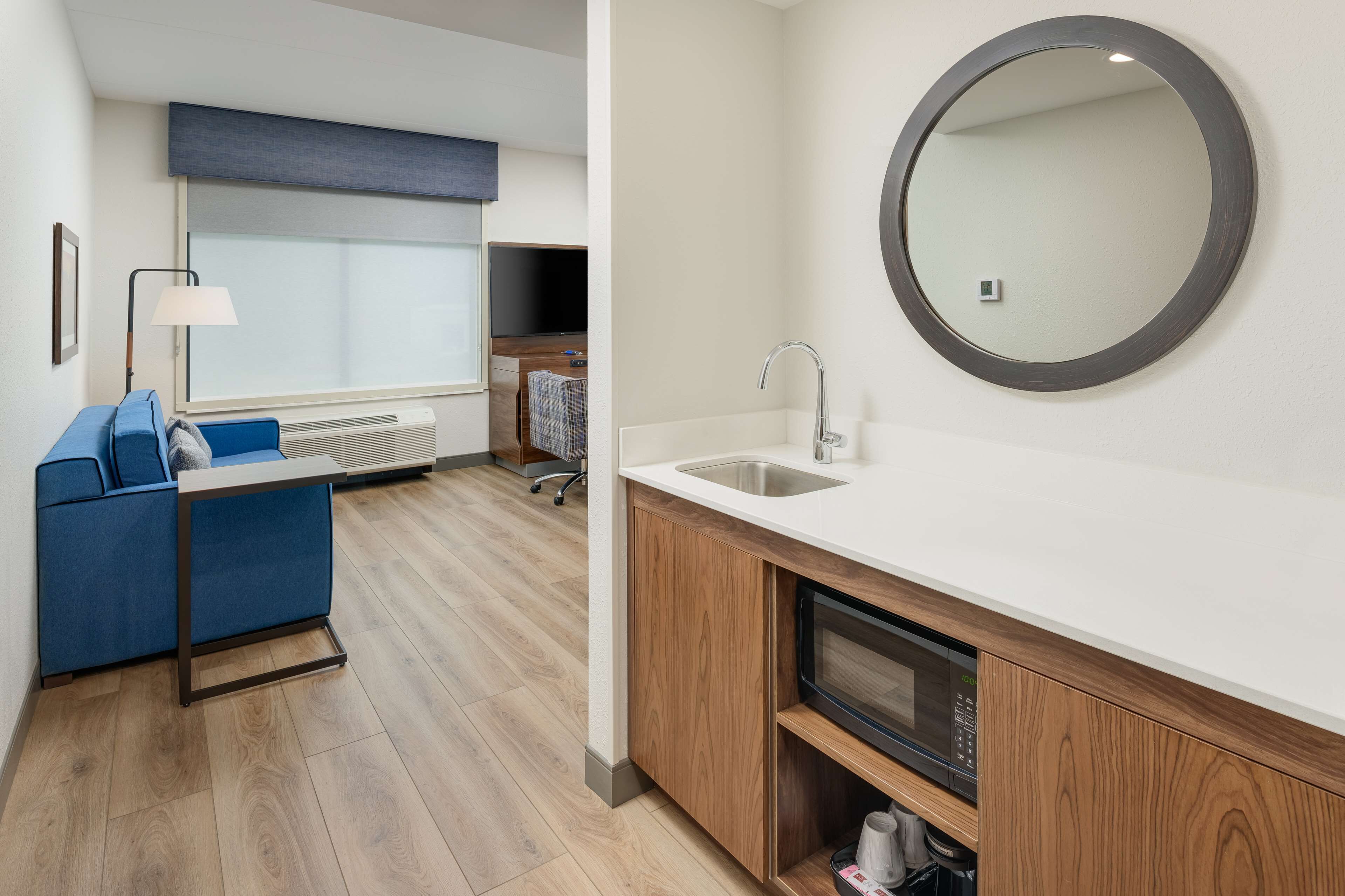 A modern kitchenette with a microwave, sink, and a round mirror.