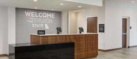 A reception desk with a "Welcome to the Peach State" sign, a digital kiosk, and a "Breakfast Area" sign.