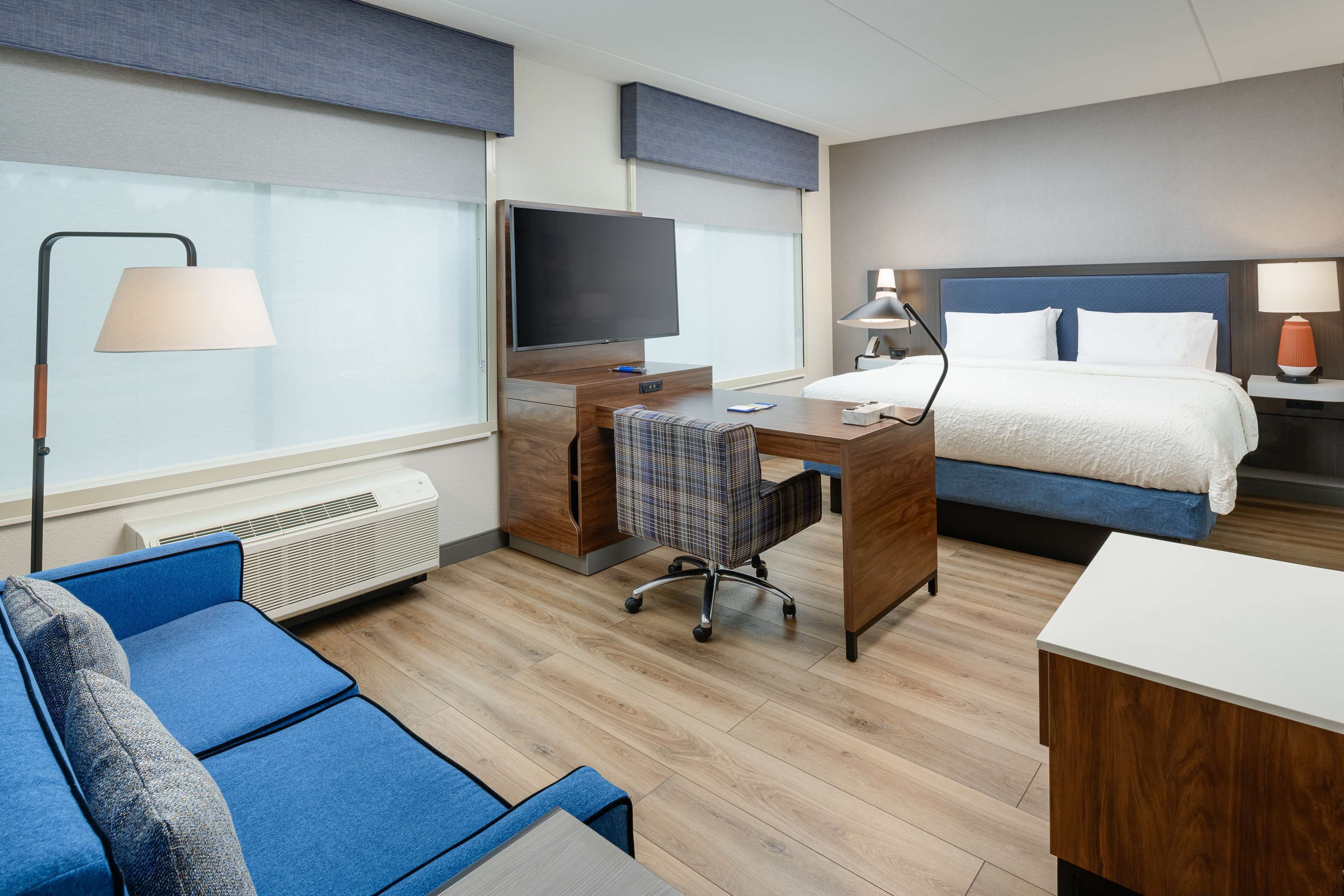 Et hotelværelse med en seng, et skrivebord med fjernsyn, en sofa og et natbord med lampe.