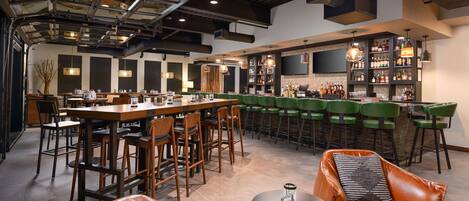 A modern bar area with high ceilings, exposed ductwork, and a variety of seating options including bar stools and a leather couch.