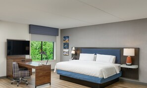 A hotel room with a bed, desk, chair, TV, and artwork on the walls.