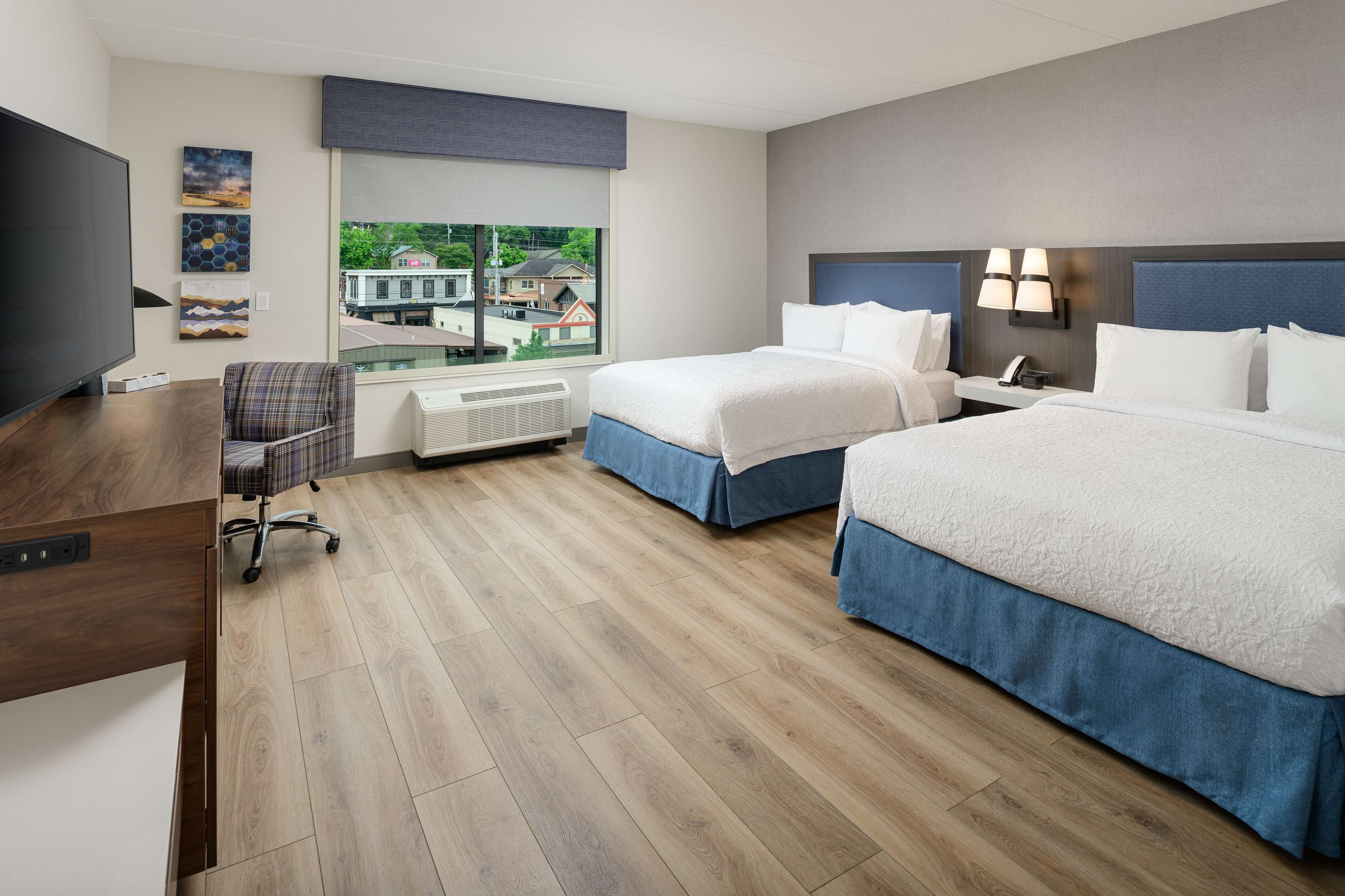 A hotel room with two beds, a desk, a chair, and a TV.