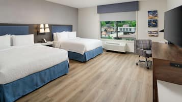 A hotel room with two beds, a desk, a chair, a TV, and a window with a view of buildings.