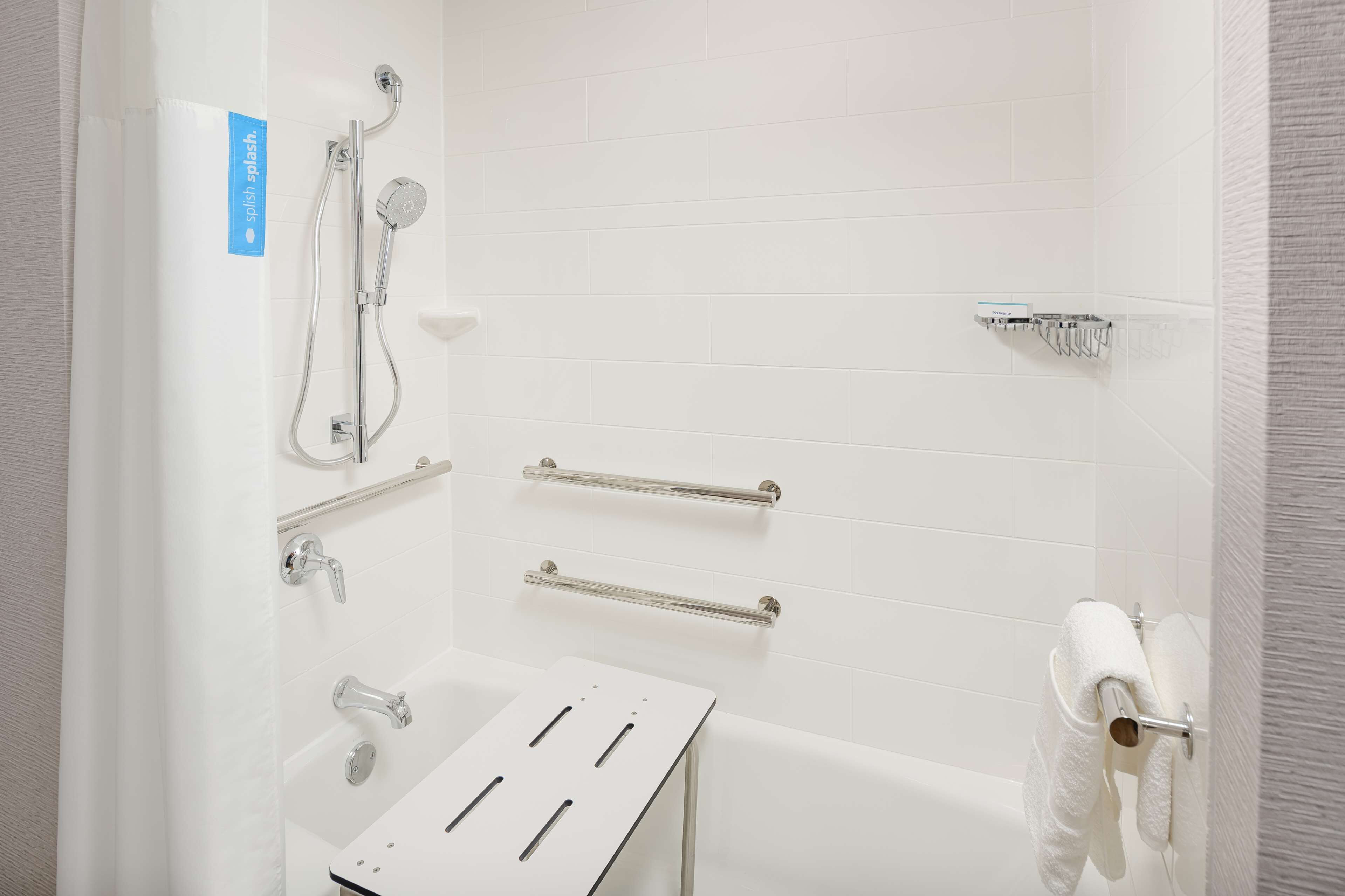 Une salle de bain moderne équipée d’une douche, de barres d’appui, d’un porte-serviettes et d’un support à papier toilette.