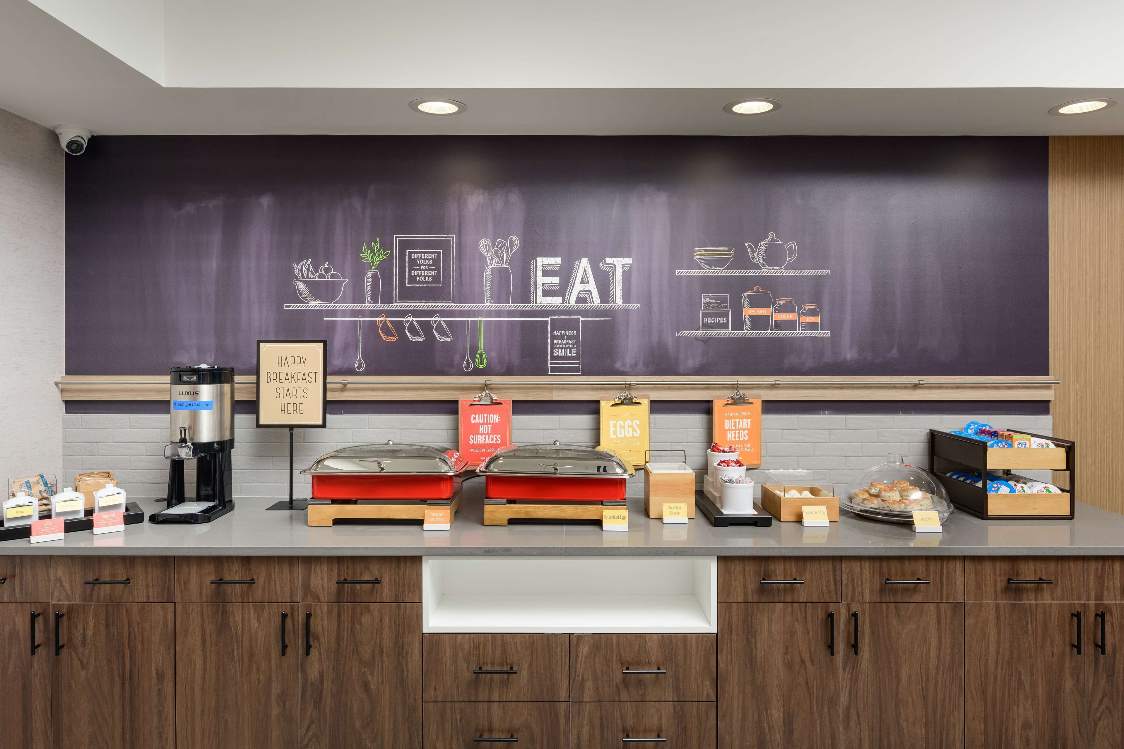 A breakfast bar with a chalkboard wall displaying food-related drawings and text, a coffee machine, and various breakfast items on display.
