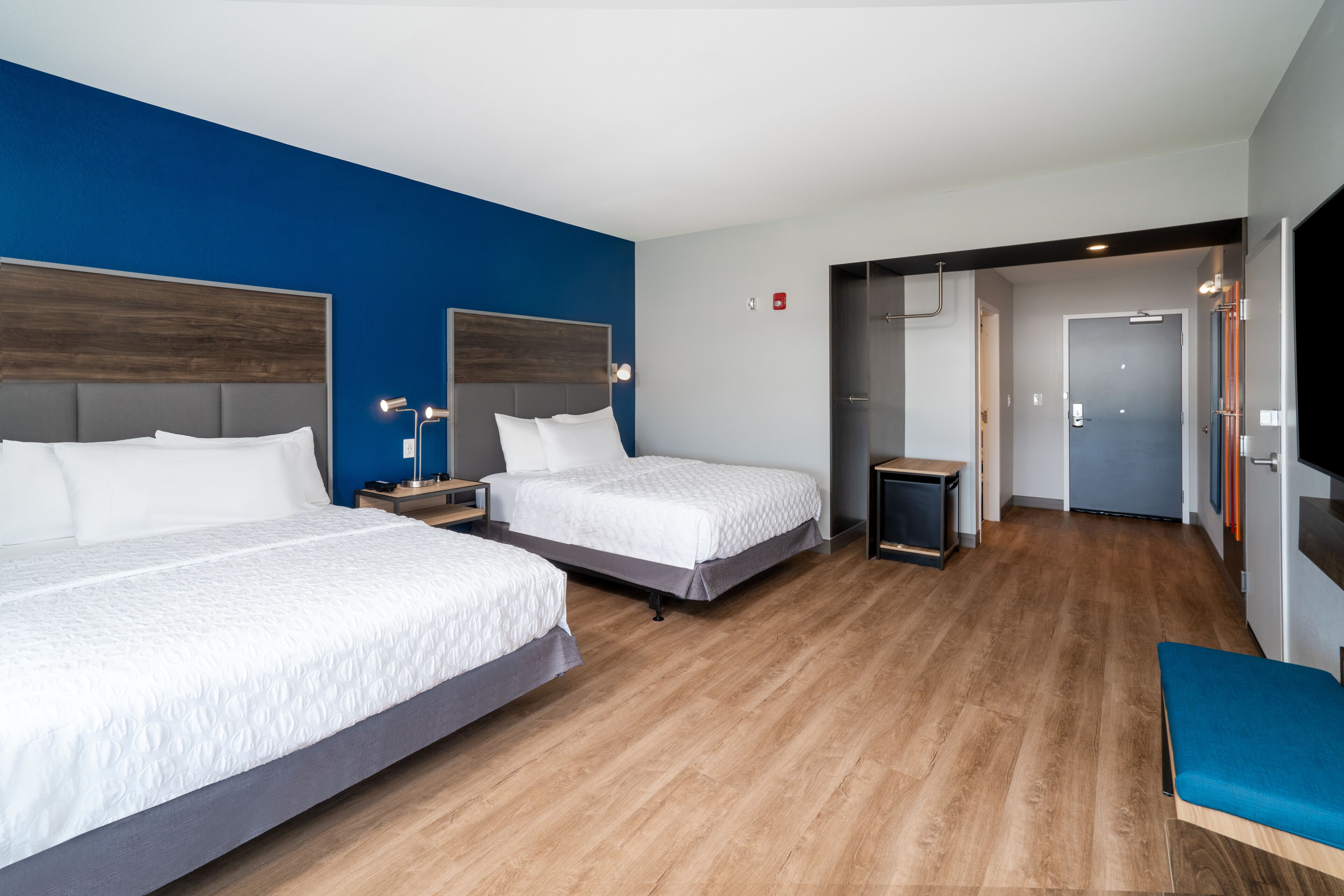 Een hotelkamer met twee bedden, een blauwe accentmuur, een houten vloer, een kleine tafel en een bank.