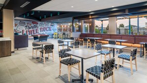 A spacious indoor area with multiple tables and chairs, a large mural on the wall, and large windows offering a view of the outside. - Tru by Hilton North Little Rock (North Little Rock)
