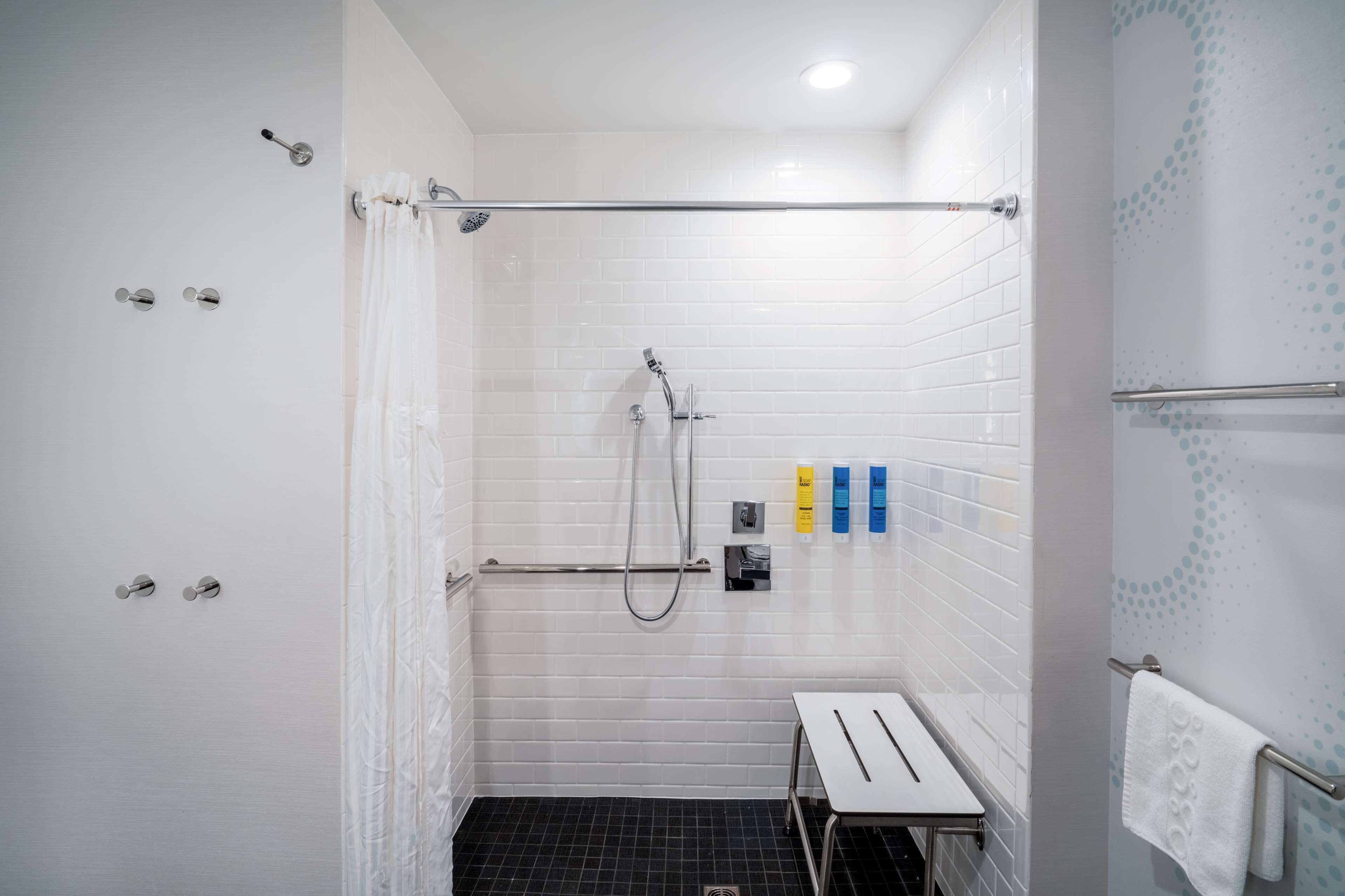 Un baño moderno con paredes de azulejos blancos, una ducha con puerta de vidrio, un banco y artículos de aseo en la pared.