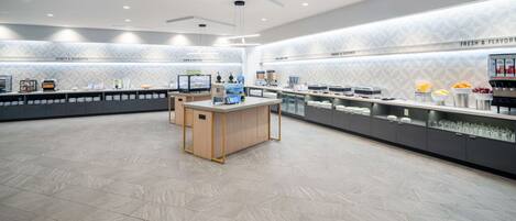 A modern, spacious cafe with a clean, geometric tile floor and a central wooden table.