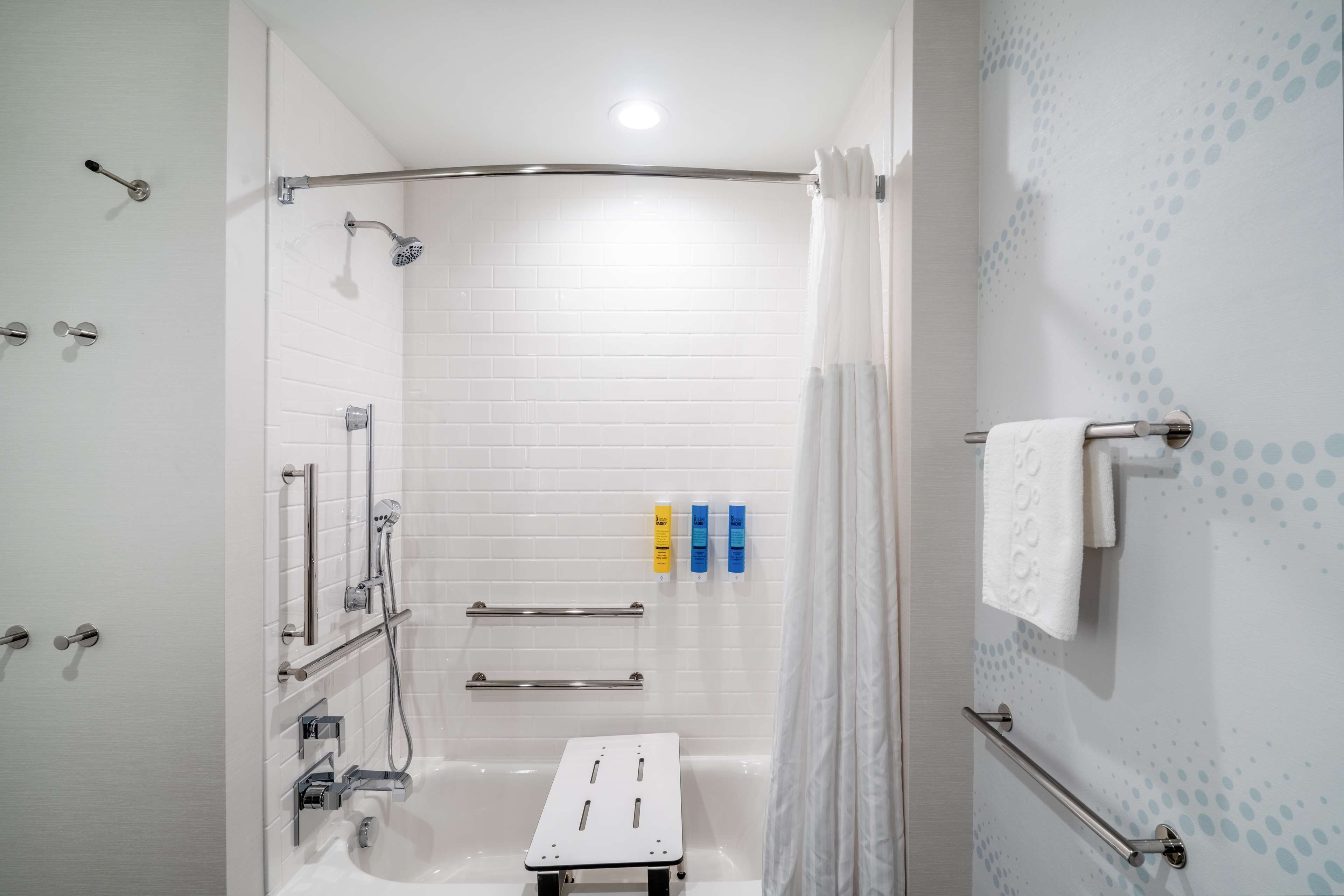 A modern bathroom with a walk-in shower, grab bars, a white sink, and a towel rack.