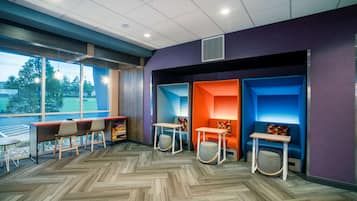A modern indoor space with a herringbone-patterned floor, a long table with chairs, and colorful seating areas with built-in benches.