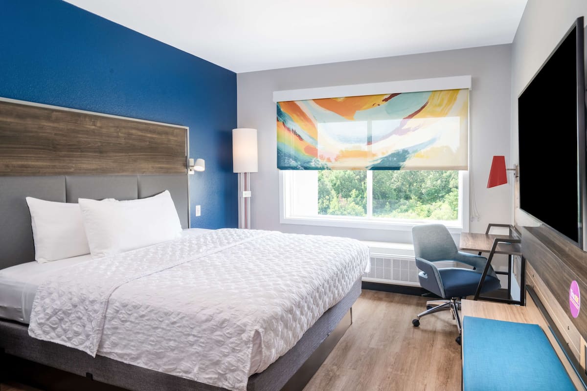 Una habitación de hotel moderna con una cama grande, un escritorio y una ventana con vistas a zonas verdes.
